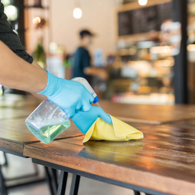 Waiter cleaning table with disinfectant spray and Microfiber cloth in cafe covid-19 preventing.